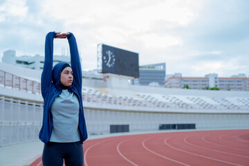 A young asian Muslim woman wearing a black hijab is exercising and running at an outdoor stadium in the morning. Modern Muslim woman concept,  Muslim woman sport concept, Islam