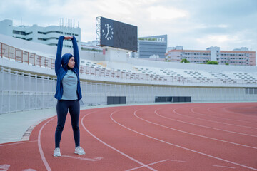 Fototapeta premium A young asian Muslim woman wearing a black hijab is exercising and running at an outdoor stadium in the morning. Modern Muslim woman concept, Muslim woman sport concept, Islam