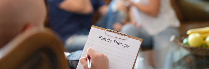Family therapist takes notes on his paper while listening to couples discuss problems.