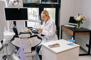 Wide shot of friendly pediatric dentist bonding with adorable child girl, talking and explaining dental procedure. Unrecognizable kid learning about healthy teeth and maintaining oral hygiene