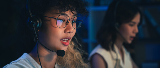 Woman consultant wearing microphone headset of customer support phone operator at night office.