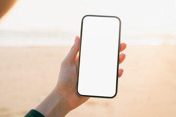 Hand holding smartphone on the beach, mobile mockup of blank screen, Take your screen to put on advertising. Summer vacation concept.