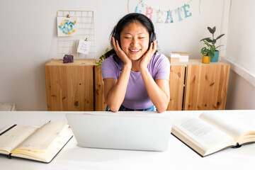 Happy Chinese woman relaxing listening to music with wireless headphones at home.Teen girl...