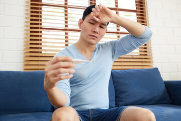 young man have a high fever from checking a digital thermometer measure body temperature at home
