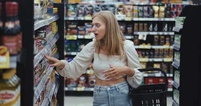 overprice blonde woman check out product from the shelf in search of right one grocery department in hypermarket and have perplexity by price. Female immediately return product on shelf overprice