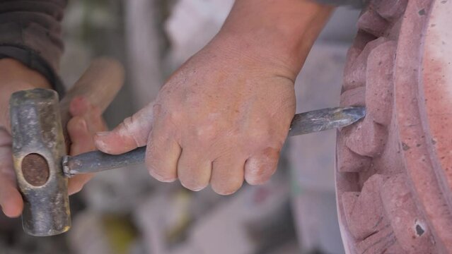 senior man, using his craft skills, to carve the stone and shape, natural pink quarry stone sculpture
