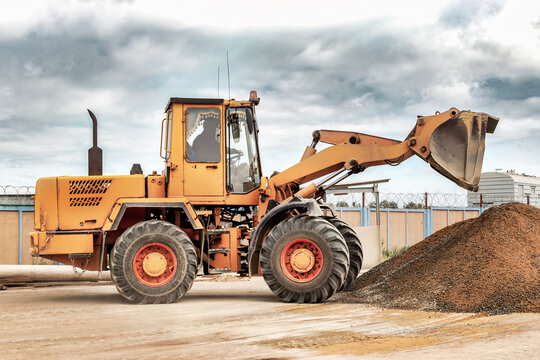 Powerful wheel loader or bulldozer at the construction site. Loader transports sand in a storage bucket. Powerful modern equipment for earthworks and bulk handling.