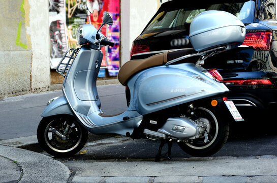 retro style metallic Italian made scooter or moped parked on asphalt road. storage box. asphalt sidewalk. grunge stucco house exterior elevation. modern transportation and lifestyle
