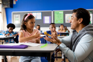 Happy diverse male teacher teaching girl using sign language in elementary school class