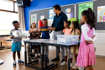 Happy diverse male teacher and children with ecology items in elementary school class