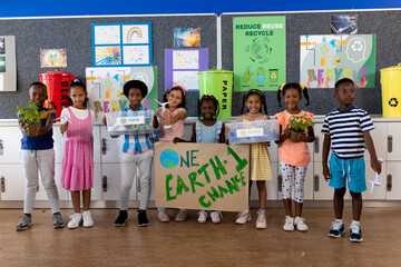 Portrait of happy diverse children with ecology items and plants in elementary school class