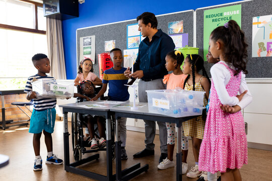 Happy diverse male teacher and children with ecology items in elementary school class