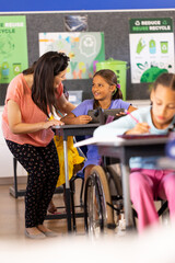Diverse female teacher and schoolgirl using tablet in elementary school class