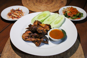 Ayam taliwang or taliwang chicken, a traditional roasted chicken dish from Lombok usually served with beberuk and water spinach plecing. Served with white plate on a wood background