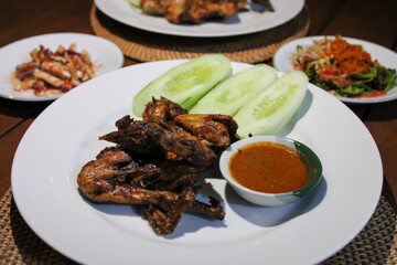 Ayam taliwang or taliwang chicken, a traditional roasted chicken dish from Lombok usually served with beberuk and water spinach plecing. Served with white plate on a wood background