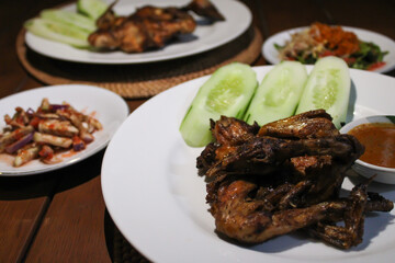 Ayam taliwang or taliwang chicken, a traditional roasted chicken dish from Lombok usually served with beberuk and water spinach plecing. Served with white plate on a wood background