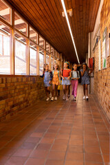 Diverse happy schoolgirls with bags walking in elementary school corridor