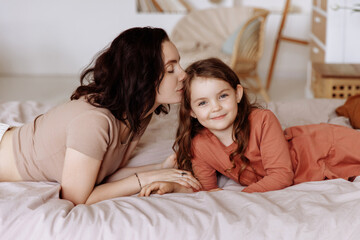 Happy loving family. Mother and her daughter girl play and hug while lying on the bed in a cozy bedroom.