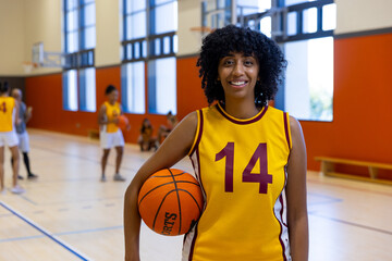 Portrait of happy biracial female basketball players holding and playing basketball at gym - Powered by Adobe