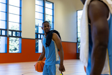 Happy african american male basketball players talking with towels at gym