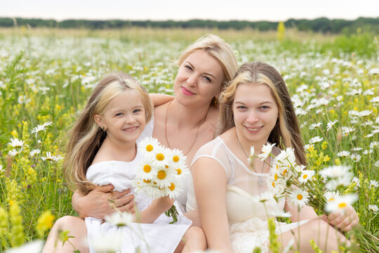 Family on nature on a summer sunny day. Mom with daughters in a chamomile field. Mom with daughters in white dresses. Image with selective focus.