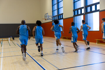 Diverse male basketball players running and warming up at gym