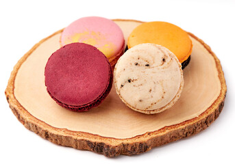 4 colorful macarons (pink, red, orange and cream-brown) placed on wooden plate isolated on white background.