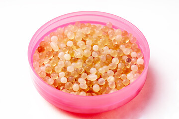 White and orange silica gel granules on pink dish isolated on white background. Desiccant to absorb any moisture.