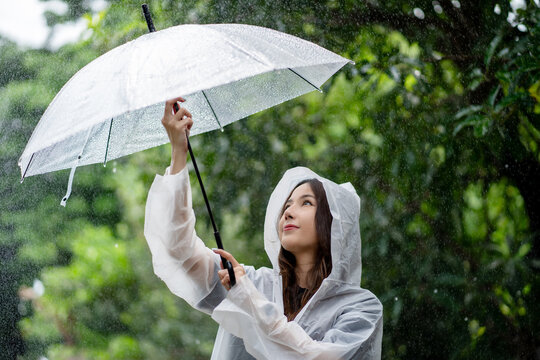 A cheerful young woman smiles in a raincoat in the rain in the middle of nature.