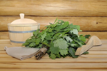 A fresh oak broom with traditional bath accessories lies on a wooden bench in a log sauna interior. 