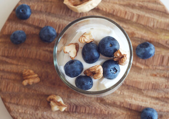 Yogurt with blueberries and walnuts in a glass on a board