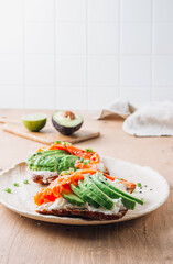Healthy breakfast sandwiche with salmon, cream cheese and avocado on wooden table.