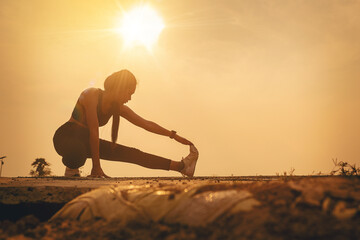 Silhouette of Woman warming up, stretching her muscle at the road track outdoor with sunset...