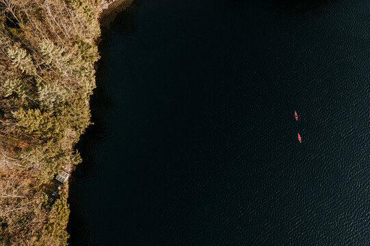 Aerial view two kayaks paddling along forested lake shoreline, Maine