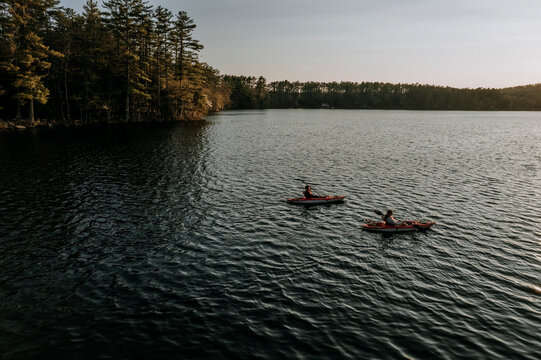 Two kayakers paddle on a pond surrounded by forest in Maine