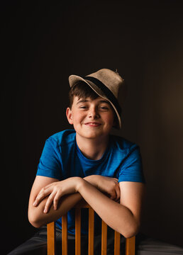 Portrait of happy boy wearing fedora hat sitting backwards on chair.