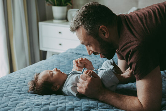 Dad is talking to the baby on the bed holding his hands