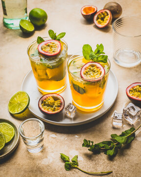 Two passion fruit mojito cocktail drinks on tray with lime and mint.