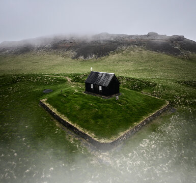 Shabby black church surrounded by hills on misty day