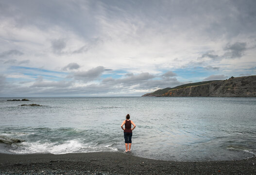 Woman standing on edge of the ocean in Newfoundland, Canada.