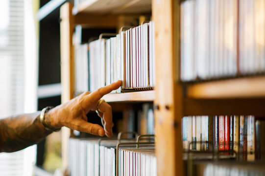 man searching through cds on a bookshelf with his hand