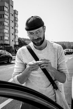 A young stylish man rolling a cigarette in the street.