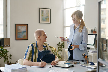 Obraz premium Young pregnant businesswoman talking to client in office while she filling documents at table