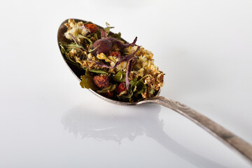 Dry tea from herbs, flowers, berries, seeds and bark is poured into a silver metal spoon on a gray...