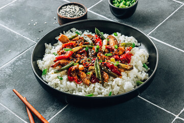 Stir fry with chicken meat, vegetables and rice in black bowl on dark tiled stone background