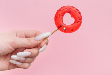 Woman female hand holding heart shaped lollipop on pink background.