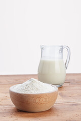 glass jug with wooden bowl full of white flour, on rustic wooden table