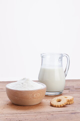 glass pitcher with wooden bowl filled with white flour and cookies on rustic wooden table
