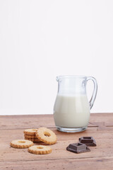 jug of milk with cookies and pieces of dark chocolate on rustic wooden table