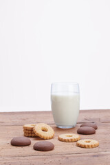 glass of milk with white and chocolate flour cookies and dark chocolate pieces on rustic wooden table